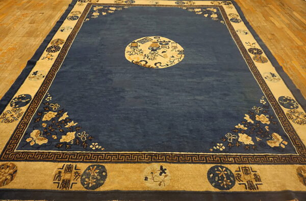 Deep blue rug with tan, ornate borders, a central medallion, and corner florals on light wood flooring.