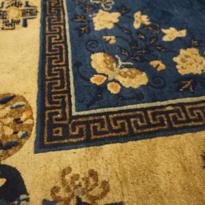 Textured blue rug featuring light floral and butterfly motifs next to a brown Greek key border on a tan ground.