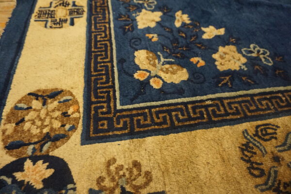 Textured blue rug featuring light floral and butterfly motifs next to a brown greek key border on a tan ground.