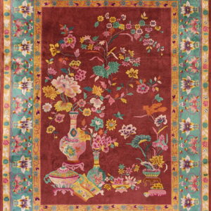 Red rug with an elaborate floral vase pattern and a complex turquoise and gold ornamental border.