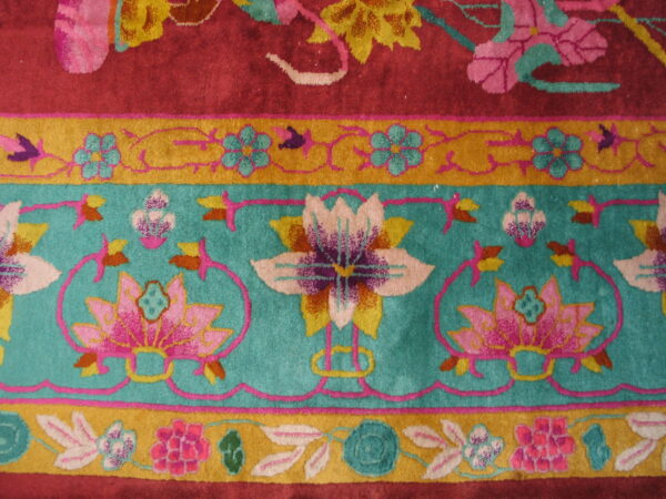 Floral pattern rug detail showing magenta field, wide teal band, and thin golden floral border.