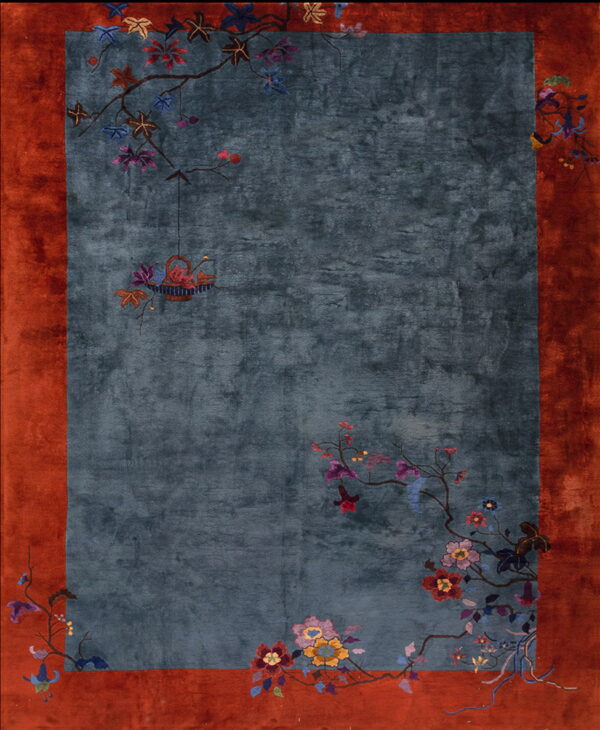 Blue rug with rust border and asymmetric floral branches and a hanging basket motif.