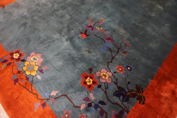 Teal high-pile rug detail showing multicolored flowers trailing from an orange border.