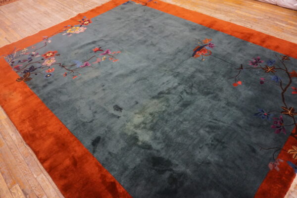 Soft teal and orange rug with bright floral branches rests on light wood planks.