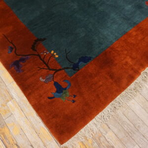 Plush teal and rust rug with a floral border pattern rests on aged wooden floorboards.