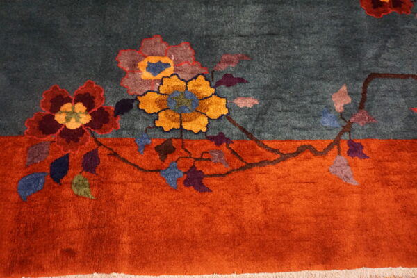 A teal rug with an orange border featuring large stylized flowers in red, gold, and purple.