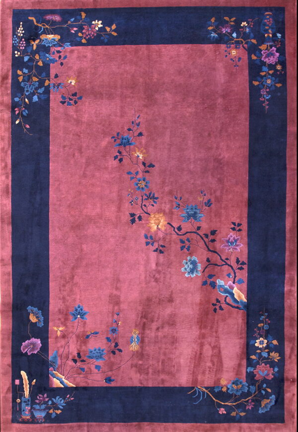 Pinkish-red rug with a navy border and blue, gold, and purple sweeping floral designs.