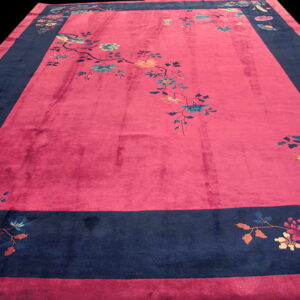 A deep magenta rug with a wide navy border, featuring scattered multicolored flowers and bird designs.