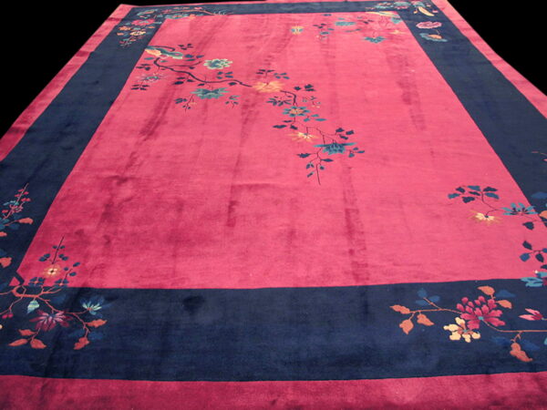 A deep magenta rug with a wide navy border, featuring scattered multicolored flowers and bird designs.