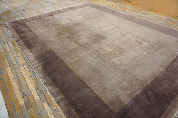 Large rectangular rug featuring a taupe field and wide stepped borders of deep brown on rustic wood floors.