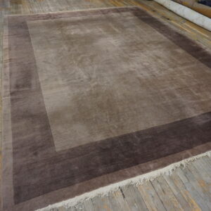 Shading taupe rug features two concentric borders of darker brown on distressed wooden floors.