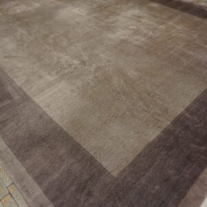 Shaded brown rug with tonal stepped borders rests on distressed gray wood flooring.