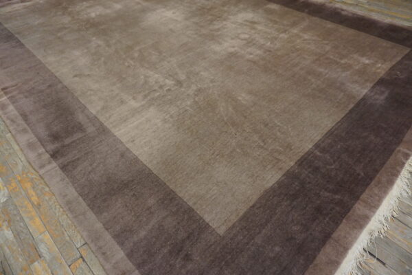 Shaded brown rug with tonal stepped borders rests on distressed gray wood flooring.