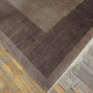 Brown geometric rug with dark borders and white fringe rests on distressed wood planks.