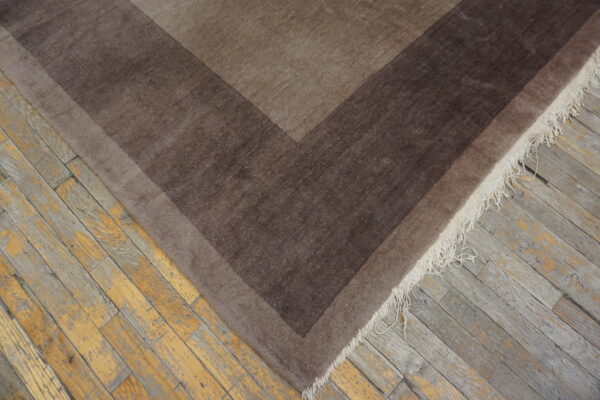 Brown geometric rug with dark borders and white fringe rests on distressed wood planks.