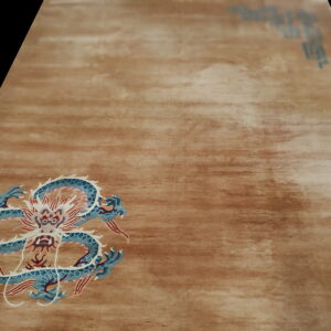 Low-angle view of a tan rug with an abrash field featuring a detailed blue, white, and red dragon motif.