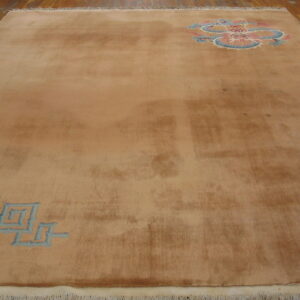 Low-pile tan area rug with a blue key pattern and a pink and blue medallion on wood planks.