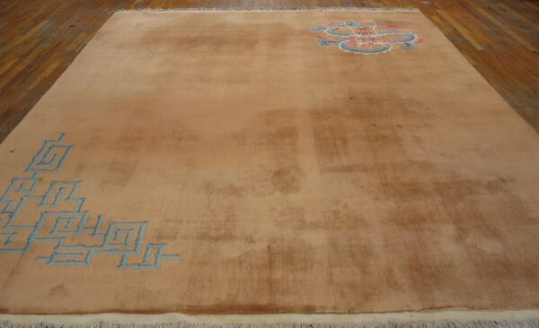 Low-pile tan area rug with a blue key pattern and a pink and blue medallion on wood planks.