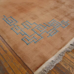 Medium pile tan rug with blue geometric pattern and fringe sits on worn wood floors.