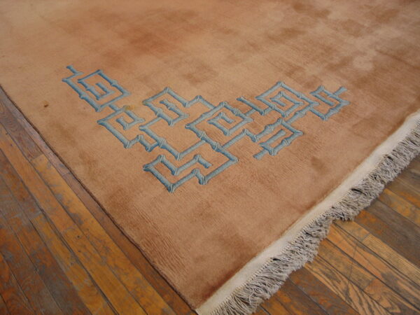 Medium pile tan rug with blue geometric pattern and fringe sits on worn wood floors.