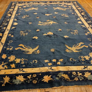 Blue rug with stylized gold birds and detailed floral borders rests on a light hardwood floor.