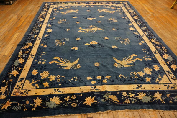 Blue rug with stylized gold birds and detailed floral borders rests on a light hardwood floor.