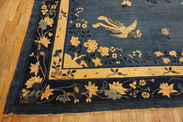 Blue rug with high contrast pale yellow floral and bird pattern on wide plank wood flooring.