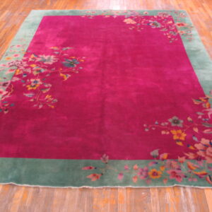 Fuchsia field rug with a wide light green floral border and multicolored vines rests on wood plank flooring.