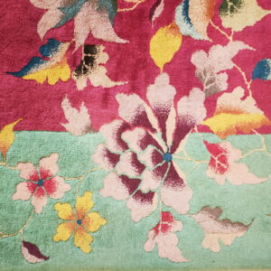 Textured rug features large multicolored floral patterns separating a magenta field from a seafoam green field.