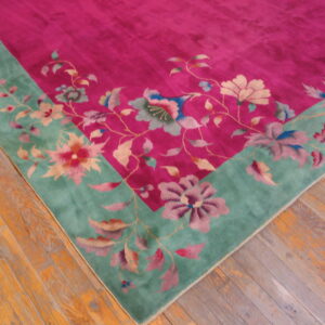 Magenta floral rug with a wide teal border featuring large flowers, lying on distressed plank wood flooring.