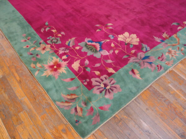 Magenta floral rug with a wide teal border featuring large flowers, lying on distressed plank wood flooring.