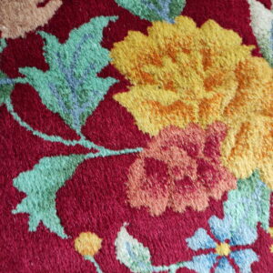 A textured, cut pile rug surface showing yellow and green flowers on a deep red background.