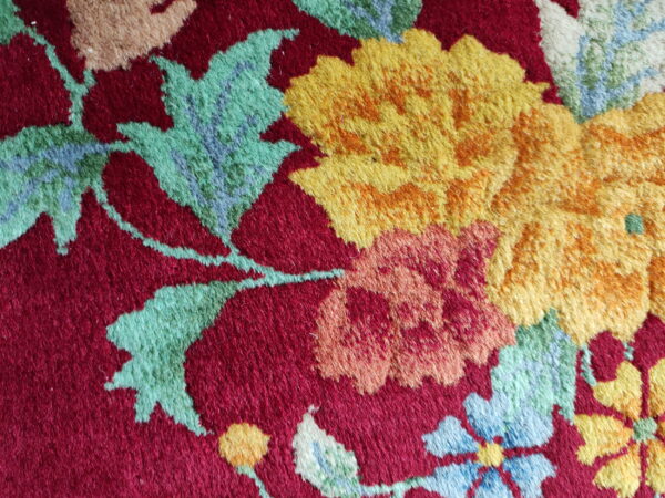 A textured, cut pile rug surface showing yellow and green flowers on a deep red background.