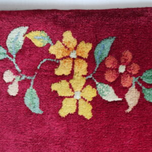 Burgundy rug detail featuring a gold, orange, and green floral vine pattern on a short, dense pile.