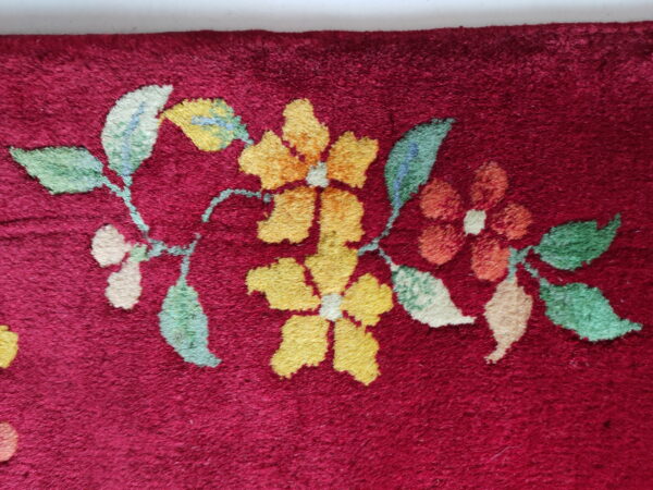 Burgundy rug detail featuring a gold, orange, and green floral vine pattern on a short, dense pile.