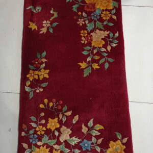 Burgundy rug featuring colorful yellow and blue floral patterns, lying on white tile flooring.