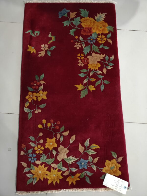 Burgundy rug featuring colorful yellow and blue floral patterns, lying on white tile flooring.