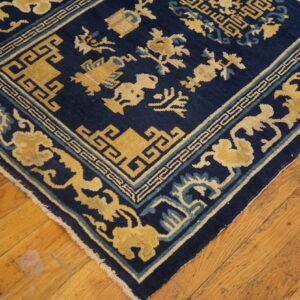 Navy and gold rug featuring geometric borders and stylized motifs rests on distressed wooden flooring.