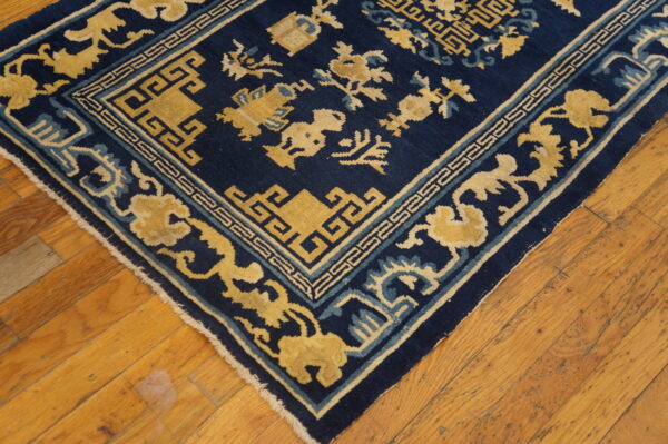 Navy and gold rug featuring geometric borders and stylized motifs rests on distressed wooden flooring.