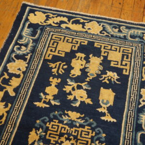 Navy blue rug with a yellow and light blue stylized pattern lies on warm, planked wood flooring.