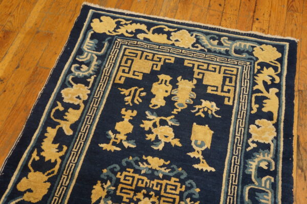 Navy blue rug with a yellow and light blue stylized pattern lies on warm, planked wood flooring.