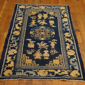 Navy blue rug with a dense yellow and light blue stylized pattern centered on wood plank flooring.