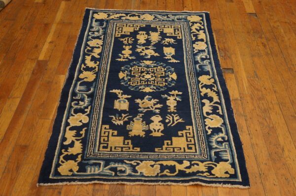 Navy blue rug with a dense yellow and light blue stylized pattern centered on wood plank flooring.