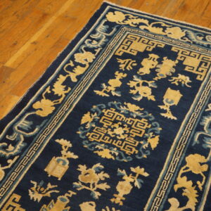 A navy blue rug with golden yellow and light blue traditional motifs rests on a wood floor.