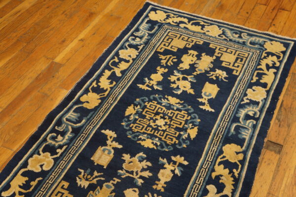 A navy blue rug with golden yellow and light blue traditional motifs rests on a wood floor.
