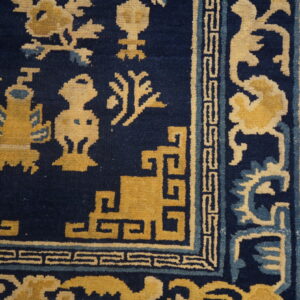 Detail of a dark blue rug featuring gold and light blue stylized symbols and a geometric border on wood plank flooring.