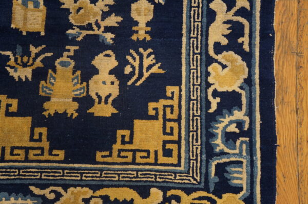Detail of a dark blue rug featuring gold and light blue stylized symbols and a geometric border on wood plank flooring.