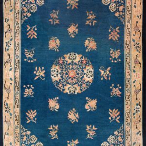 Blue rug with a tan border and scattered pink and gold floral patterns and a detailed central medallion.