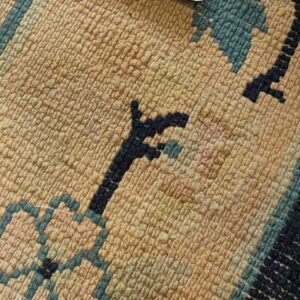 Curled low-pile tan rug with geometric patterns overlaps a high-pile dark blue rug with orange details.