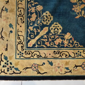 A close view of a dark teal rug with wide borders featuring gold and pink floral motifs.